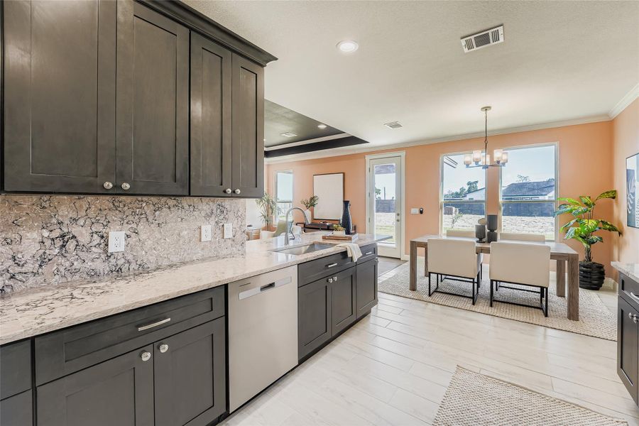 Kitchen with light stone counters, dishwasher, a chandelier, hanging light fixtures, and tasteful backsplash
