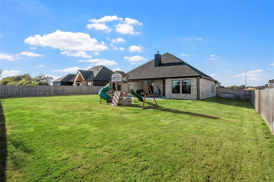 Back of house with a fenced backyard, brick siding, a chimney, and a playground Back of house with a fenced backyard, brick siding, a chimney, and a playground
