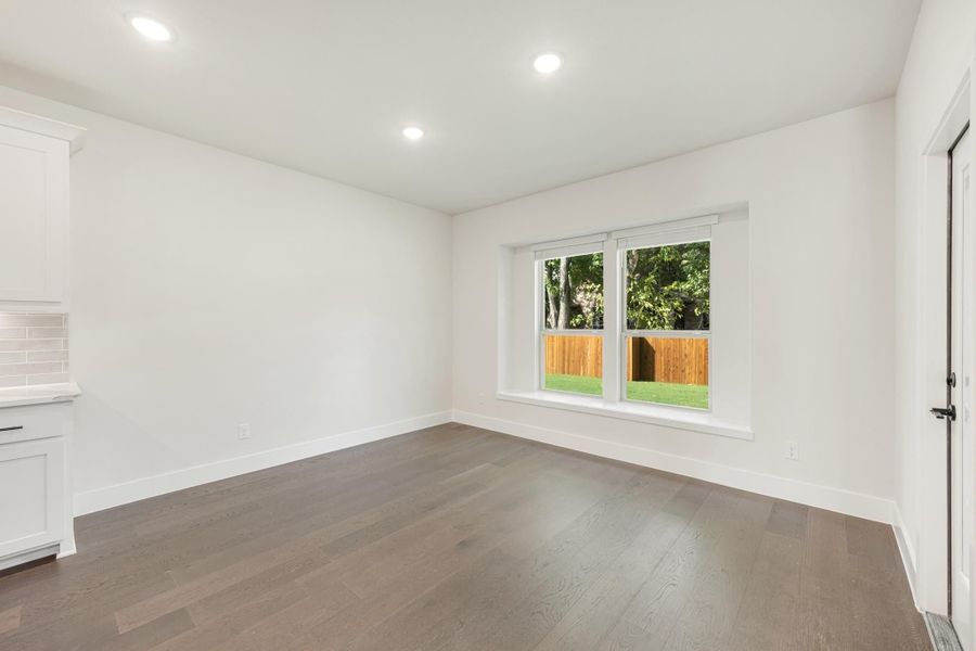 Empty room with dark hardwood floors, white walls, recessed lighting, and a double window overlooking a backyard.