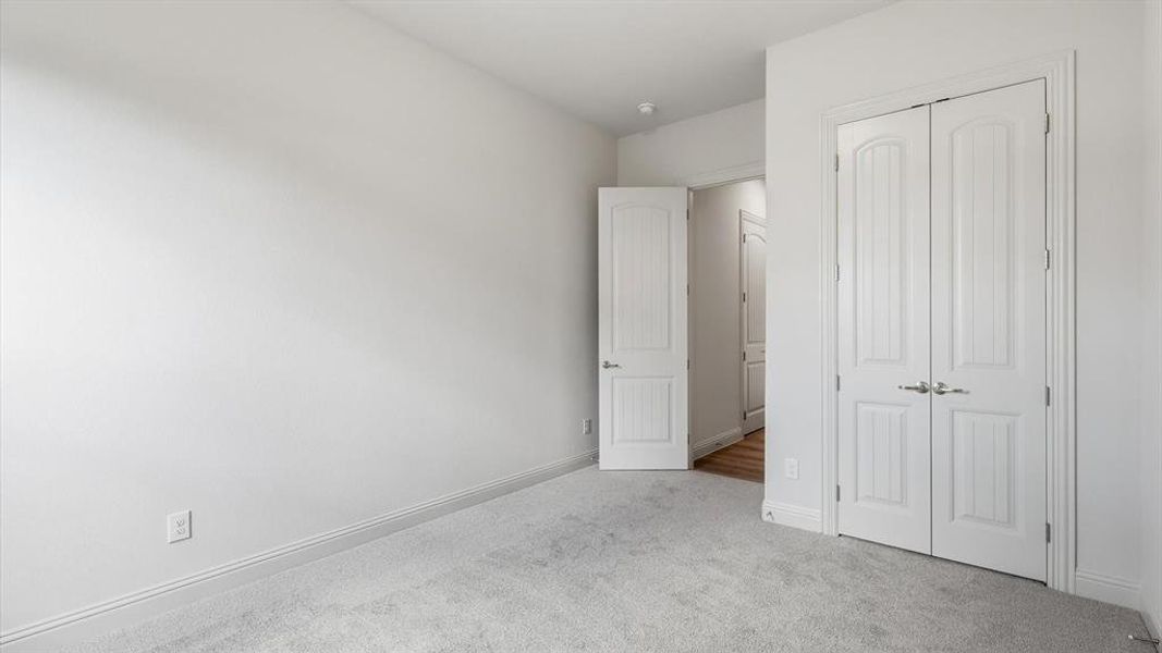Spacious room featuring light gray carpeting, white baseboards, and a pair of white paneled double doors with polished chrome hardware