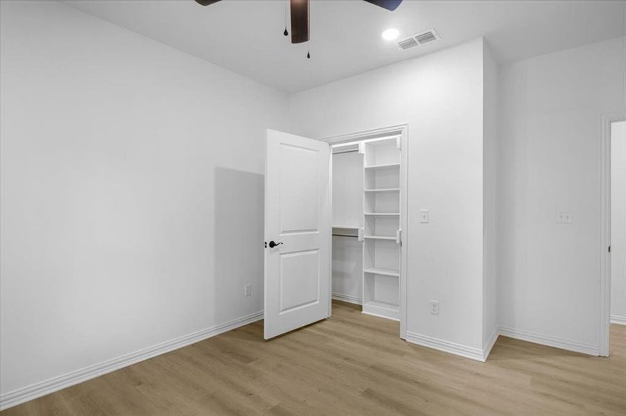 Unfurnished bedroom with a walk in closet, light wood-type flooring, and ceiling fan
