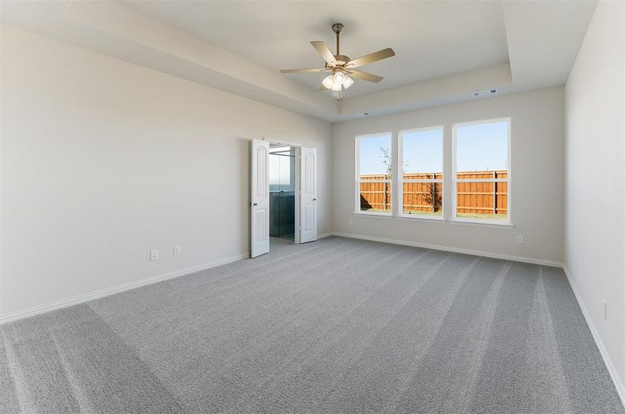 Unfurnished bedroom featuring a raised ceiling, carpet flooring, and ceiling fan