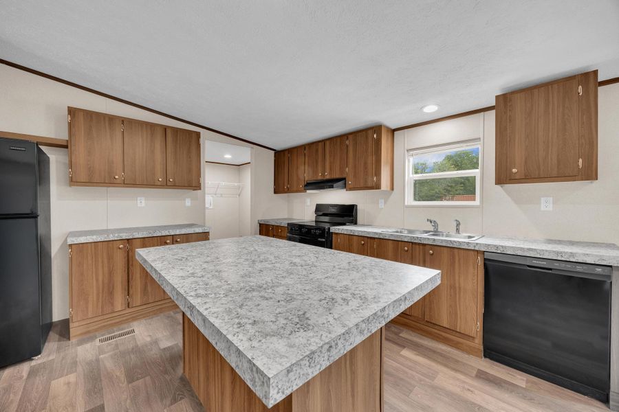 Kitchen with black appliances, a kitchen island, light countertops, brown cabinetry, and ornamental molding