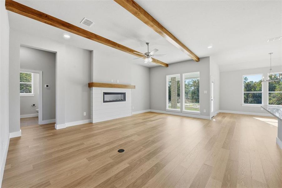 Unfurnished living room featuring a glass covered fireplace, beam ceiling, a ceiling fan, a chandelier, and light wood-style flooring Unfurnished living room featuring a glass covered fireplace, beam ceiling, a ceiling fan, a chandelier, and light wood-style flooring