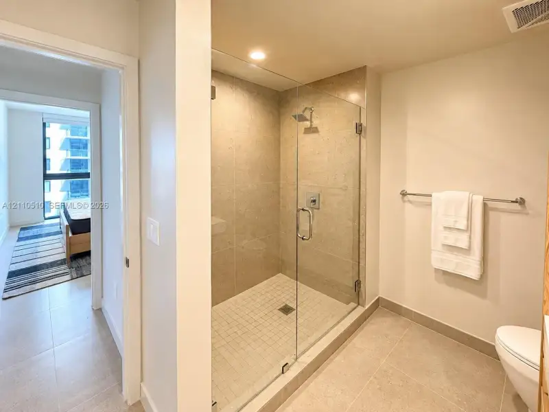 Walk-in shower featuring glass paneling, floor-to-ceiling stone-tile surround, square mosaic tile flooring, and a wall-mounted shower fixture Walk-in shower featuring glass paneling, floor-to-ceiling stone-tile surround, square mosaic tile flooring, and a wall-mounted shower fixture