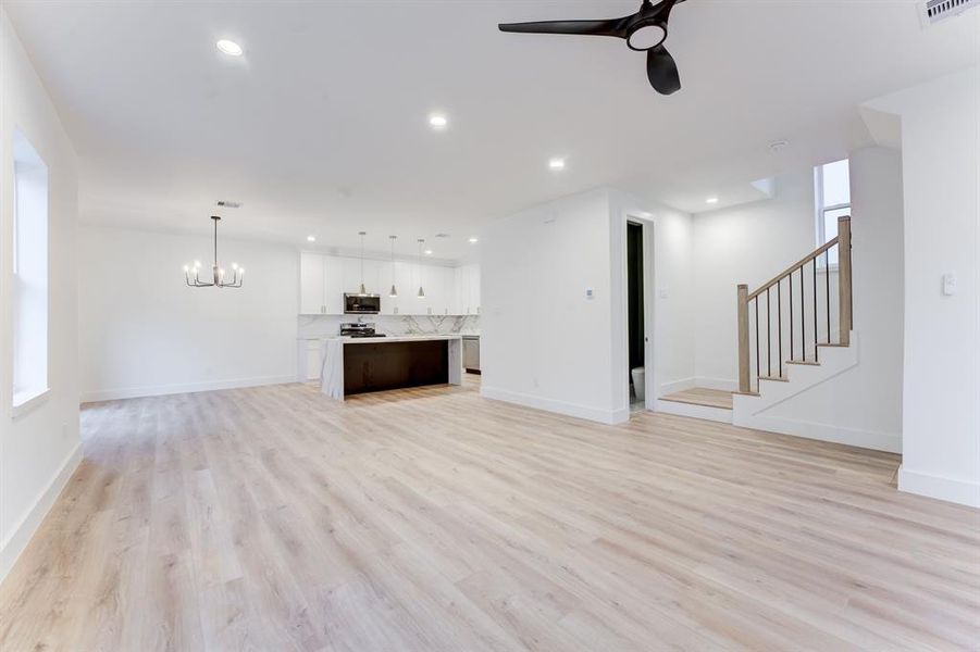 This spacious living room features an open layout with light wood flooring, modern decor, and ample natural light from large windows, ceiling fan, and recessed lighting.