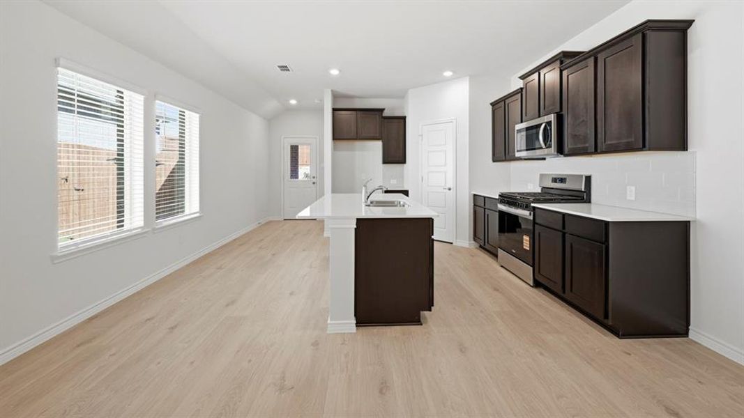 Kitchen featuring appliances with stainless steel finishes, an island with sink, recessed lighting, light wood-style flooring, and light stone counters