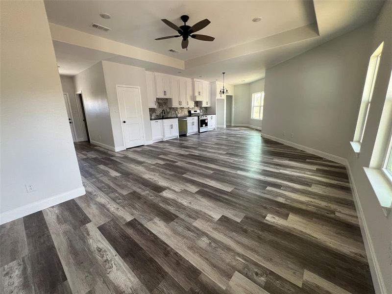 Unfurnished living room with visible vents, a sink, dark wood-style floors, baseboards, and ceiling fan