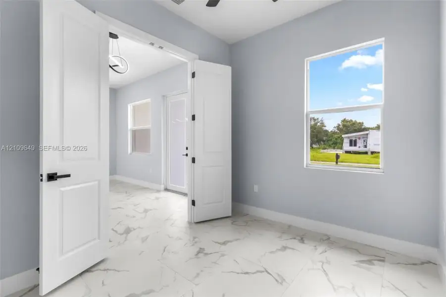 Large-format white tile flooring with grey veining, crisp neutral wall paint, multi-panel double doors with matte black hardware, and double-pane window