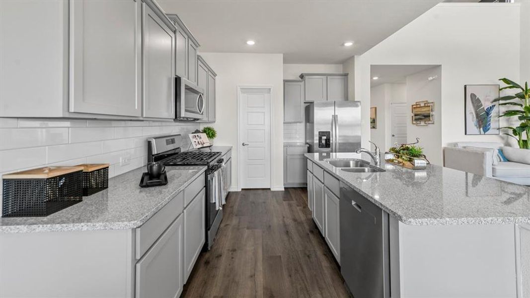 Kitchen featuring light gray cabinetry, stainless steel appliances, speckled stone countertops, a white subway tile backsplash, and wood-finish flooring