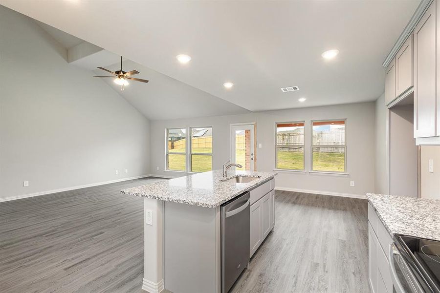 Kitchen featuring appliances with stainless steel finishes, light stone counters, sink, hardwood / wood-style floors, and an island with sink