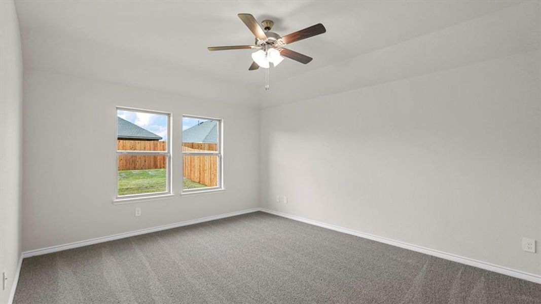 Spacious room featuring neutral carpeting, light-colored walls, white baseboards, and a ceiling fan with integrated lighting