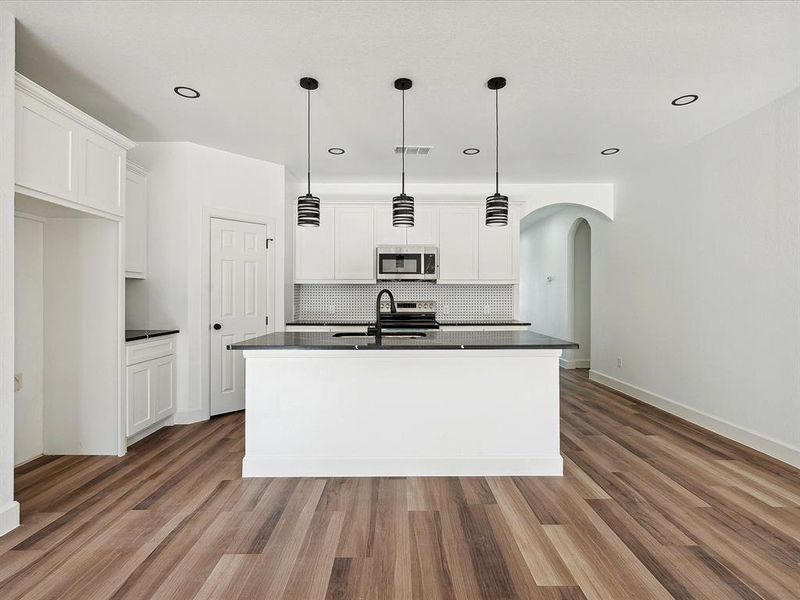 Kitchen with appliances with stainless steel finishes, white cabinetry, a kitchen island with sink, and light wood-type flooring