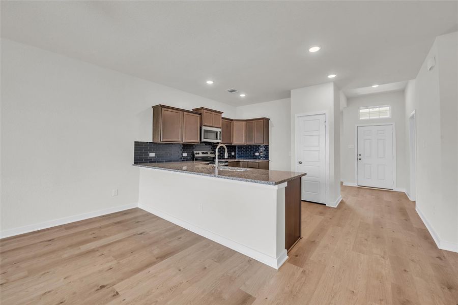 Kitchen featuring tasteful backsplash, dark stone countertops, a peninsula, recessed lighting, and light wood-type flooring Kitchen featuring tasteful backsplash, dark stone countertops, a peninsula, recessed lighting, and light wood-type flooring