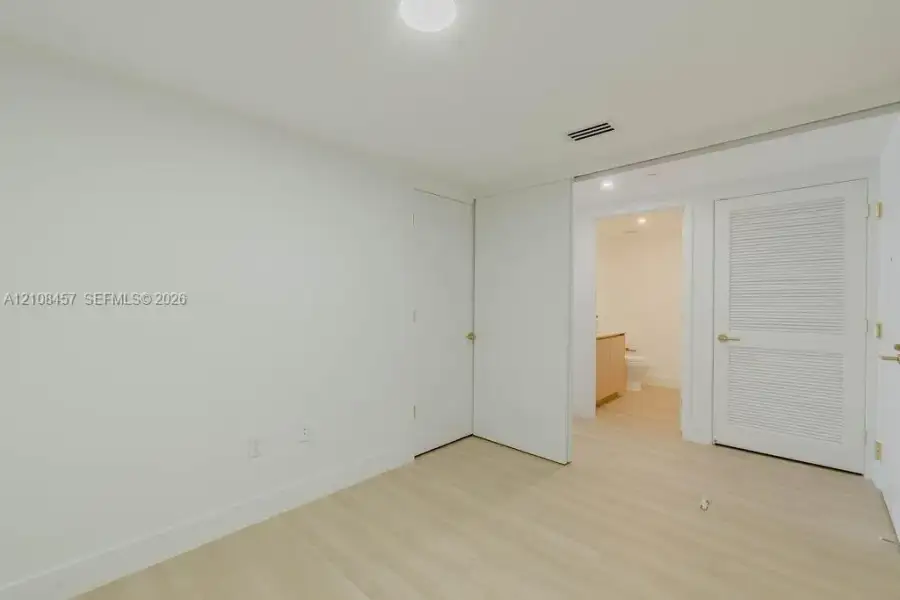 Interior space featuring wood-finish flooring, a louvered closet door, a flush-mount ceiling light fixture, and a neutral color palette Interior space featuring wood-finish flooring, a louvered closet door, a flush-mount ceiling light fixture, and a neutral color palette