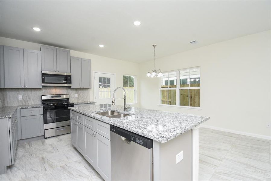 Modern kitchen with gray cabinets, stainless steel appliances, granite countertops, and an island under recessed lighting.