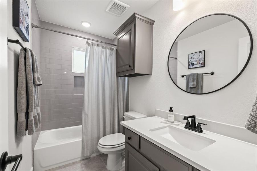 Full bath with shower / bath combo, vanity, light tile patterned floors, and a textured wall Full bath with shower / bath combo, vanity, light tile patterned floors, and a textured wall