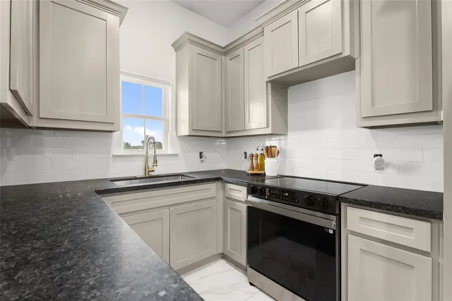 Kitchen featuring stainless steel electric range, light marble finish floors, decorative backsplash, and dark stone countertops
