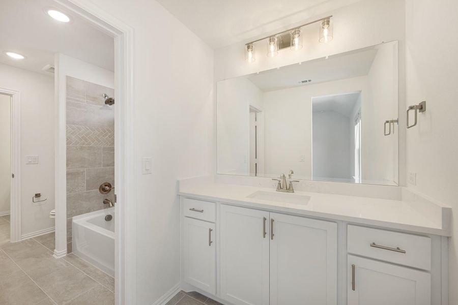 Bathroom with white vanity, large mirror, and tiled tub-shower combo with herringbone tile accent Bathroom with white vanity, large mirror, and tiled tub-shower combo with herringbone tile accent
