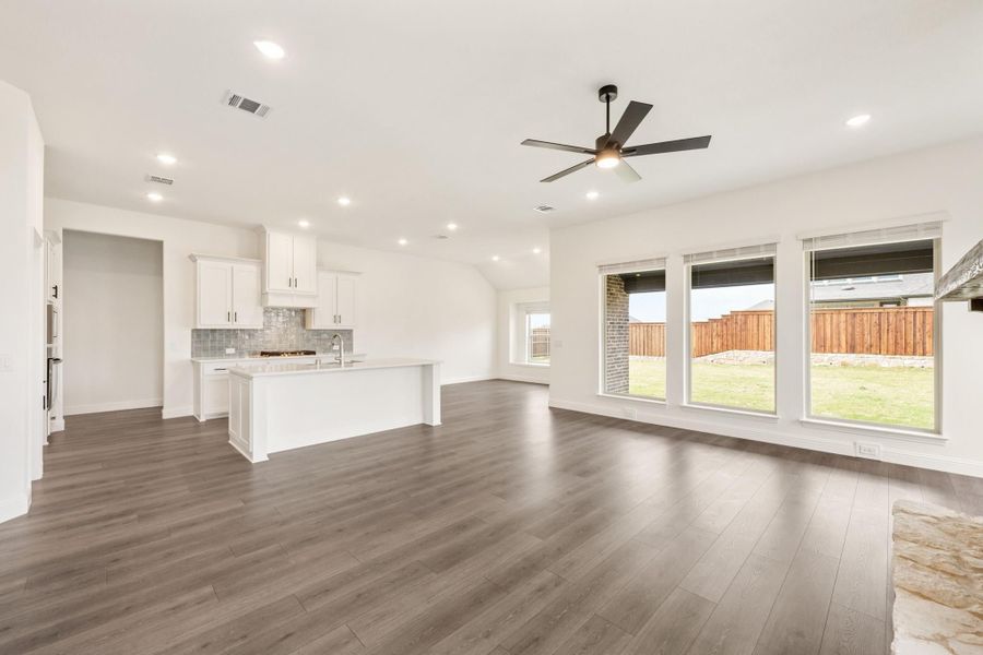 Open-concept living area and kitchen with hardwood floors, white cabinets, ceiling fan, and large backyard windows