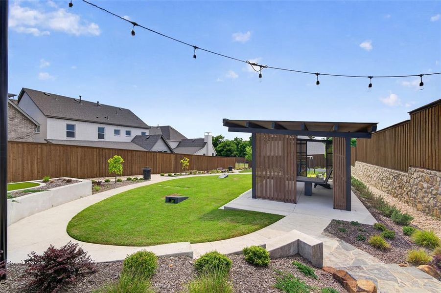Expansive outdoor space featuring a modern pergola with a built-in bench, string lighting, a manicured lawn, and stone retaining walls Expansive outdoor space featuring a modern pergola with a built-in bench, string lighting, a manicured lawn, and stone retaining walls