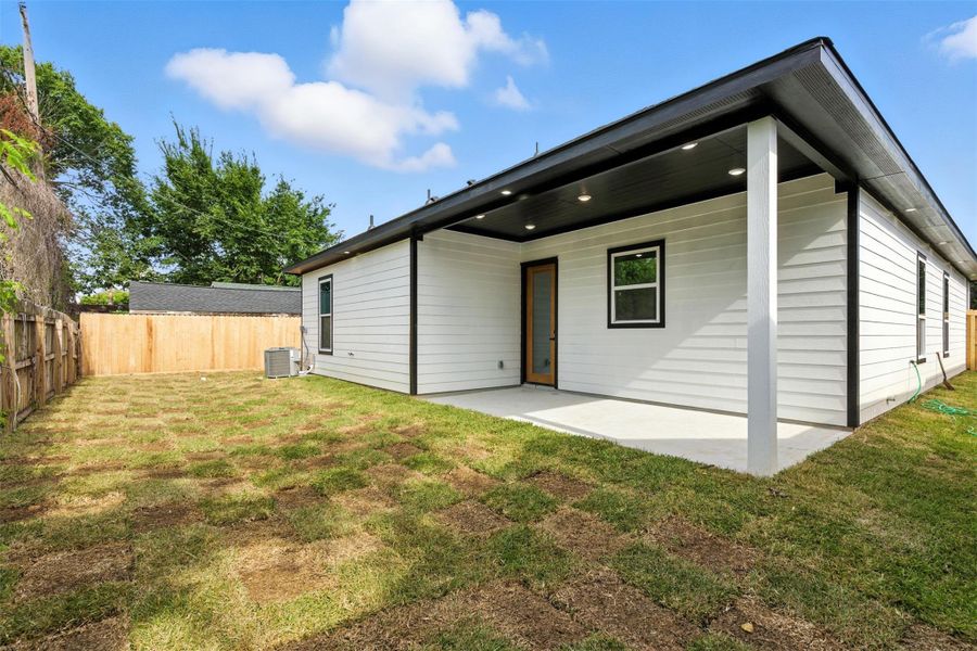 This photo showcases a modern backyard with a covered patio, fresh sod, and wooden fencing, offering a private and inviting outdoor space.