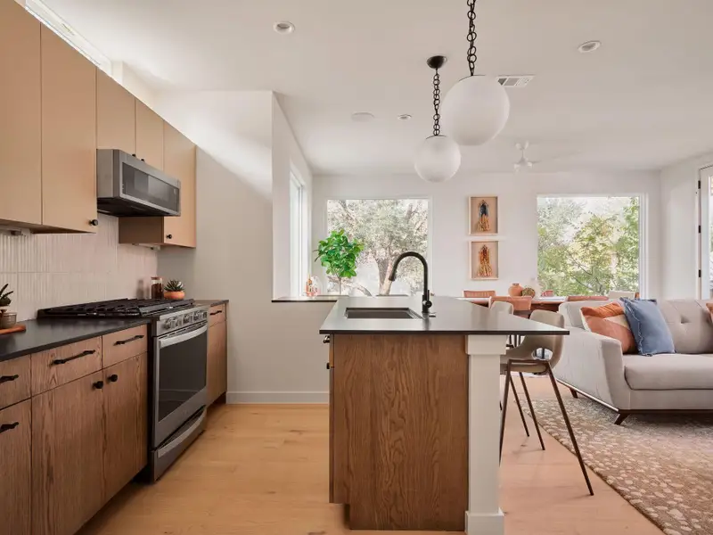Kitchen featuring dark countertops, stainless steel appliances, decorative light fixtures, open floor plan, and light wood-style flooring