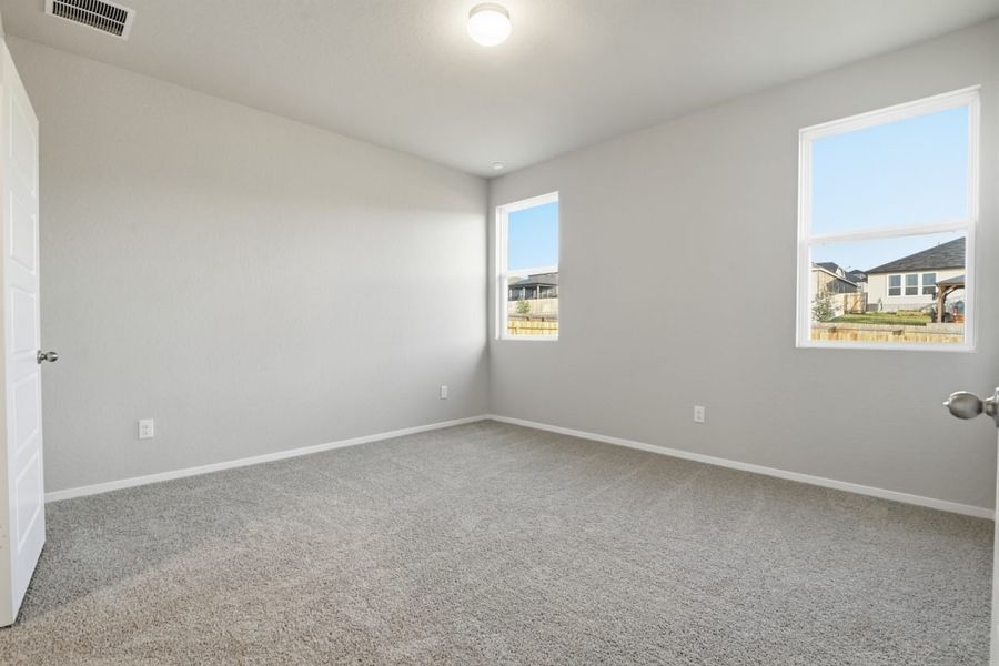 Image of a primary bedroom with light grey walls, tan carpeting and two windows