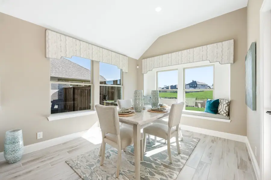 Bright dining area with vaulted ceiling, window seat, and light wood floors overlooking backyard