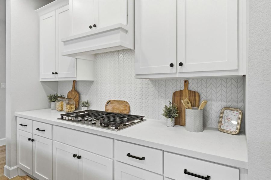 Culinary enthusiasts will appreciate the professional-style 5-burner gas cooktop accented by a designer tile backsplash, custom vent hood, extensive cabinetry, generous drawer storage, and expansive quartz workspace designed for effortless meal preparation.