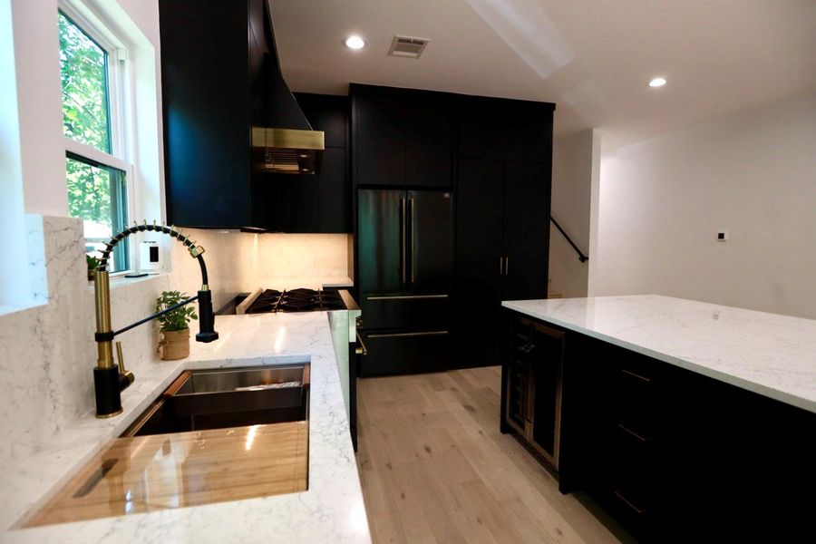 Kitchen featuring dark cabinetry, light stone countertops, high end black refrigerator, and stainless steel range with gas stovetop