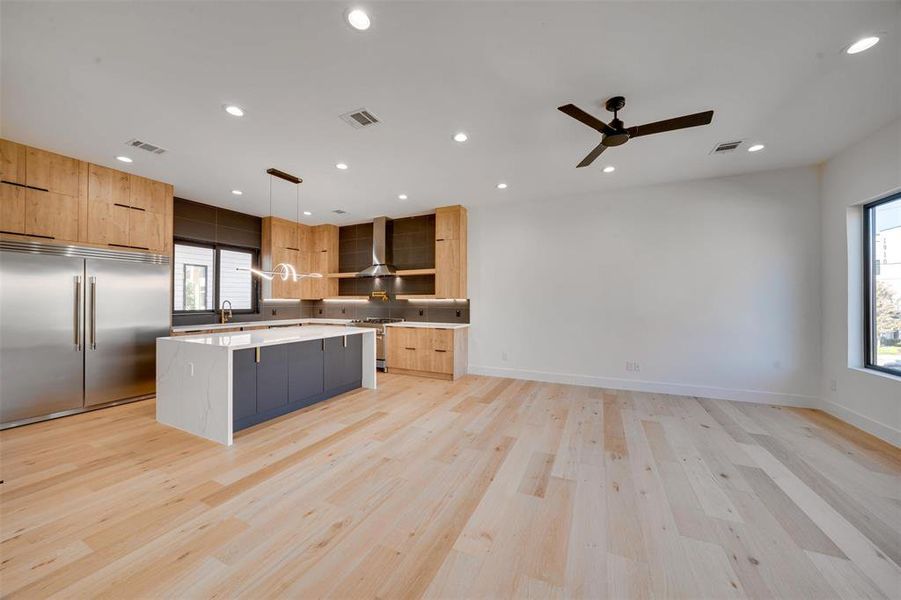 Kitchen with wall chimney exhaust hood, premium appliances, light hardwood / wood-style flooring, a center island, and hanging light fixtures