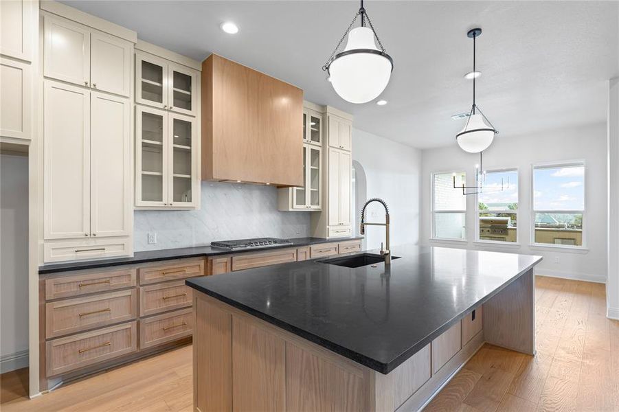 Kitchen with a large island, tasteful backsplash, light wood-type flooring, hanging light fixtures, and two tone color scheme