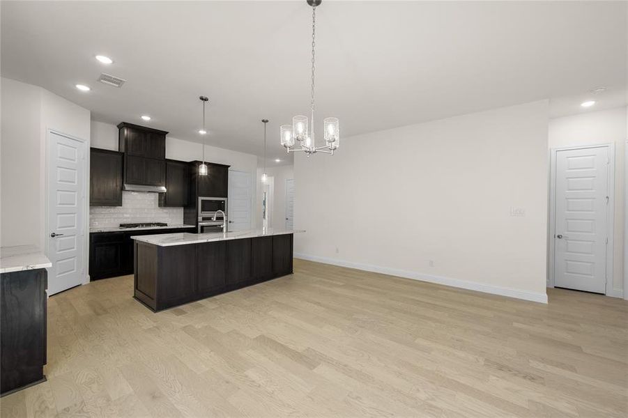 Kitchen with appliances with stainless steel finishes, light wood-type flooring, recessed lighting, tasteful backsplash, and a kitchen island with sink
