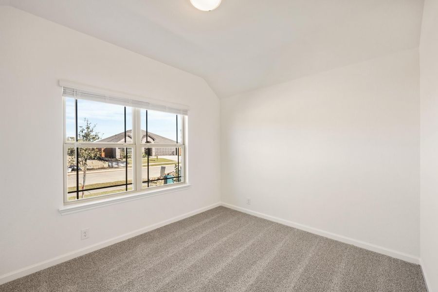 Empty bedroom with vaulted ceiling, gray carpet, and large window overlooking neighborhood street