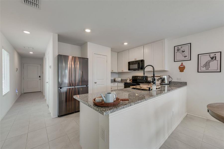 Kitchen with black appliances, light stone counters, a peninsula, light tile patterned floors, and recessed lighting Kitchen with black appliances, light stone counters, a peninsula, light tile patterned floors, and recessed lighting