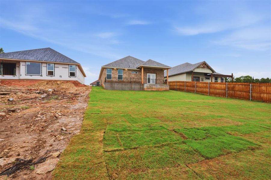 Expansive backyard featuring newly laid sod, a full privacy fence, and a brick-clad home exterior with an elevated patio Expansive backyard featuring newly laid sod, a full privacy fence, and a brick-clad home exterior with an elevated patio
