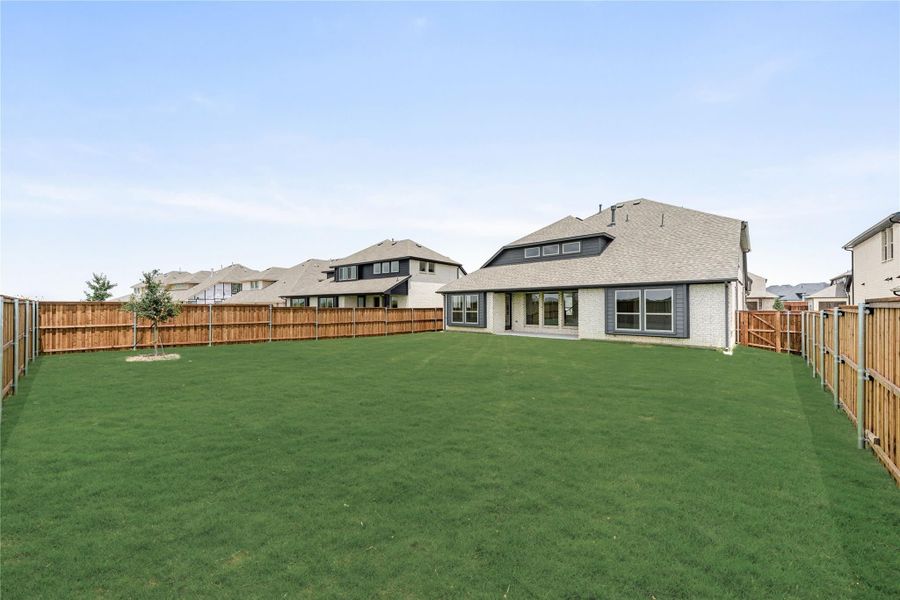 Large backyard with green lawn, wood privacy fence, and brick home with covered patio