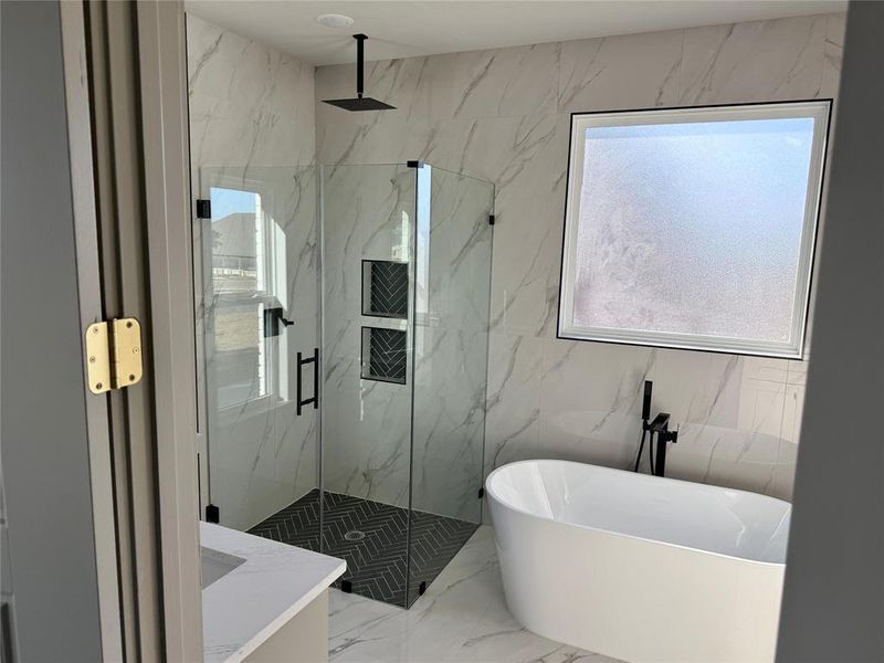 Bathroom featuring marble tiled flooring, a freestanding bath, a marble finish shower, and stone wall