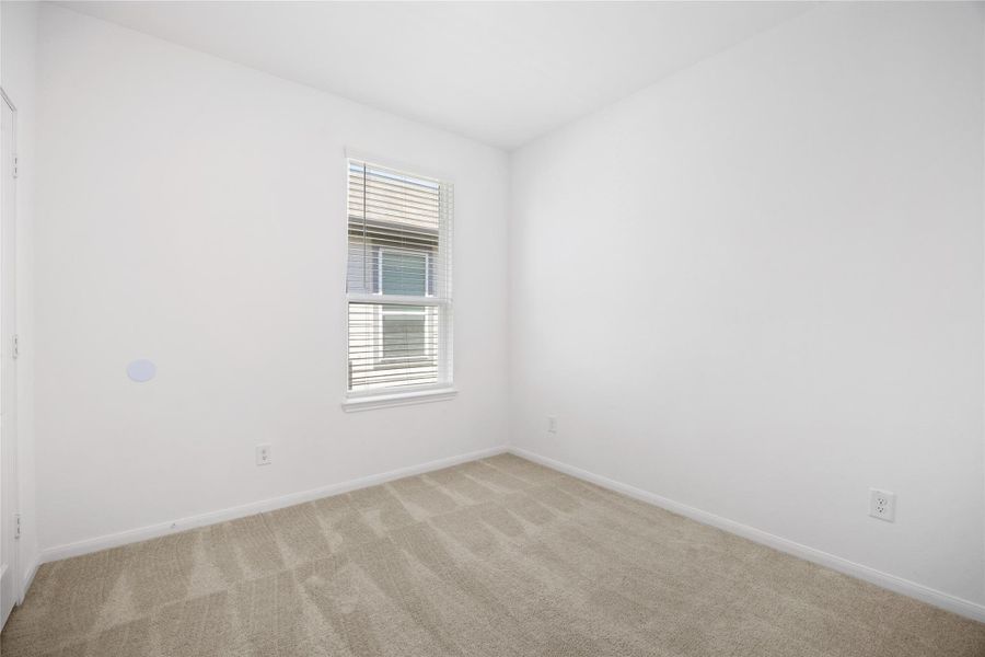 bright, small room with white walls and a window allowing natural light. The carpeted floor adds warmth, and the space is ideal for a cozy bedroom or home office.
