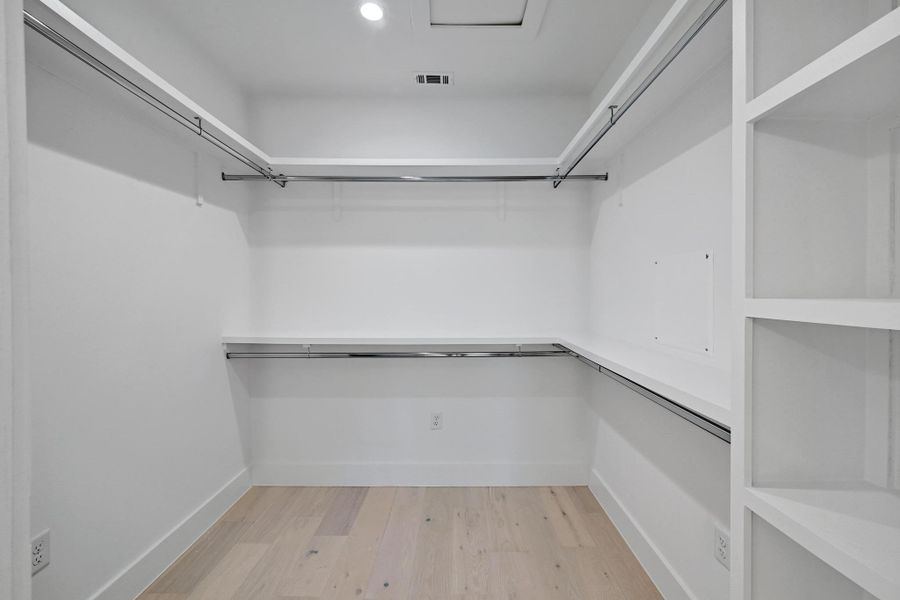 Spacious primary  closet with light wood-style floors and visible vents