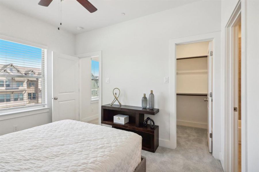 Bedroom with ceiling fan, a walk in closet, light carpet, and multiple windows