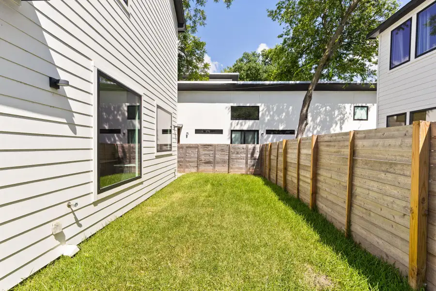 A fenced backyard space provides a private green retreat between modern residential structures.