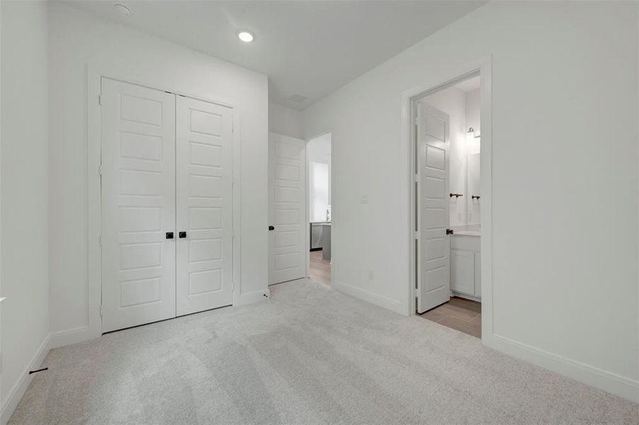 Bedroom featuring light gray carpet flooring, white walls, and a pair of white paneled bifold closet doors with black hardware Bedroom featuring light gray carpet flooring, white walls, and a pair of white paneled bifold closet doors with black hardware