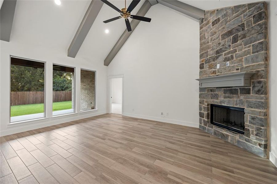 Unfurnished living room with high vaulted ceiling, a fireplace, beamed ceiling, light wood-type flooring, and a ceiling fan