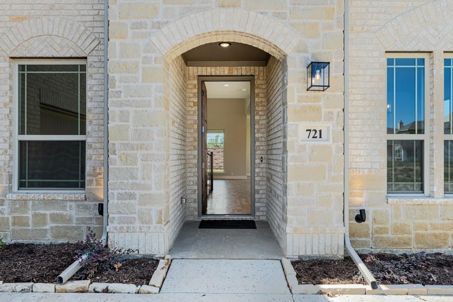 Home entrance with arched stone surround, glass front door, and wall sconce light at number 721