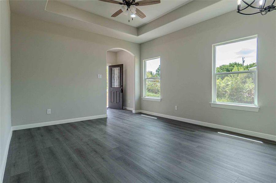 Empty room featuring hardwood / wood-style flooring, a raised ceiling, and ceiling fan with notable chandelier