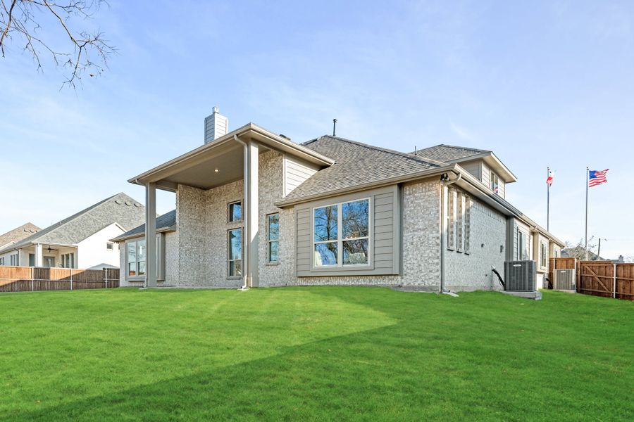 Rear exterior of two-story brick home with covered patio, large windows, and fenced backyard lawn Rear exterior of two-story brick home with covered patio, large windows, and fenced backyard lawn