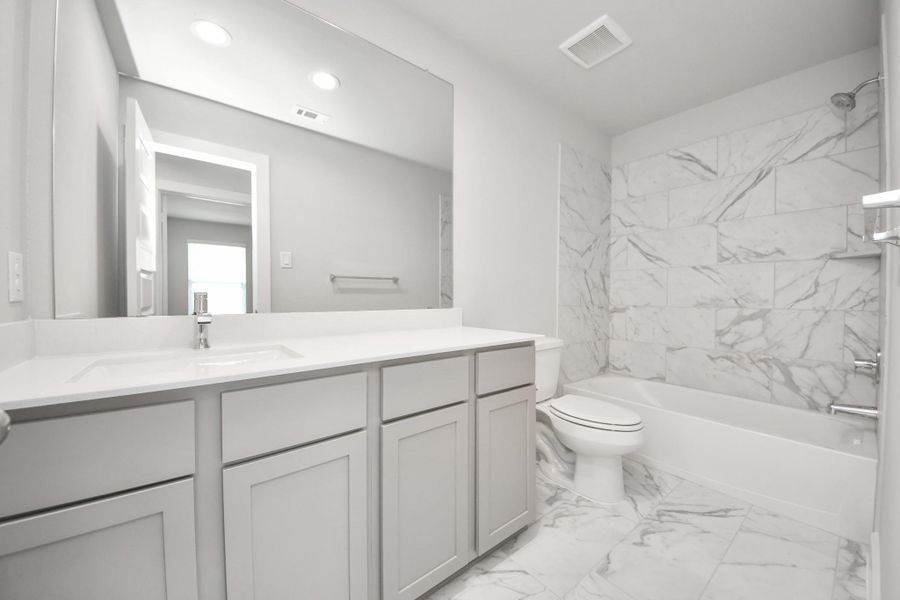Secondary bath features tile flooring, bath/shower combo with tile surround, light stained wood cabinets, beautiful light countertop. Sample photo of completed home with similar floor plan. Actual colors and selections may vary.