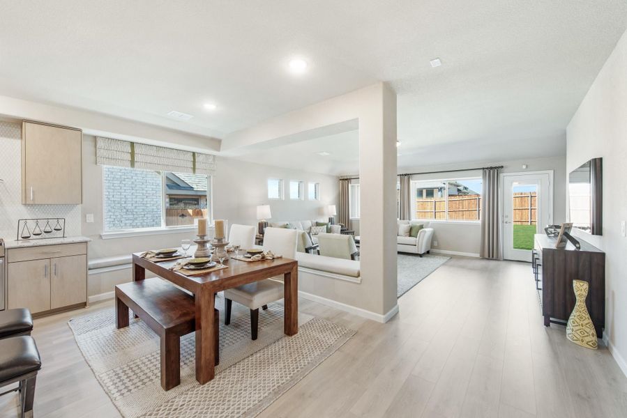 Open-concept dining area with wood table and bench, flowing into living room with light hardwood floors Open-concept dining area with wood table and bench, flowing into living room with light hardwood floors